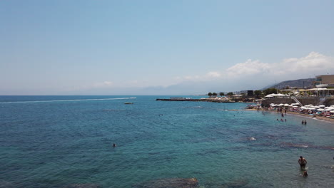 Playa-De-Cielo-Azul-Claro-En-Creta,-Grecia,-Con-Una-Multitud-Moderada-Relajándose