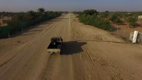 Drone-Shot-of-4X4-Truck-Speeding-Along-Dusty-Desert-Road-with-Palm-Trees