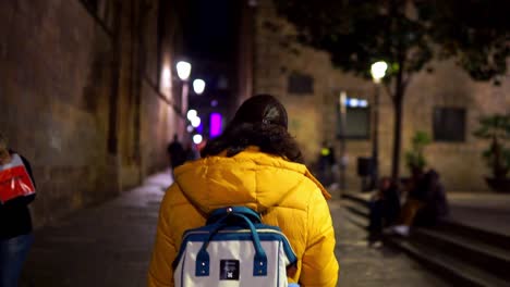 Close-Up-Shot,-Women-in-Yellow-Jacket-Walking-the-Streets-of-Barcelona,-Spain,-during-the-night,-People-Walking,-Street-Light-In-the-background