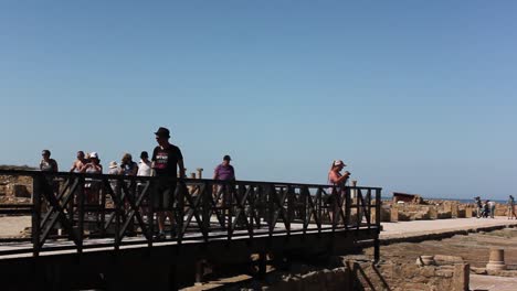 Man-walking-along-railing-in-Paphos-Archaeological-park-surrounded-by-group-of-tourists
