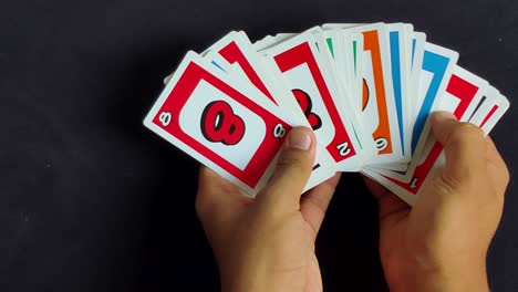 Männliche-Hände-Legen-Bunte-Uno-Spielkarten-Auf-Einem-Schwarzen-Tisch-Aus