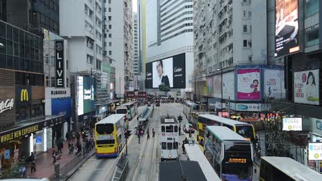 Double-Deck-Tram-And-Buses-On-A-Busy-Street-In-Downtown-Sheung-Wan-District-Of-Hong-Kong-With-Pedestrians-Crossing