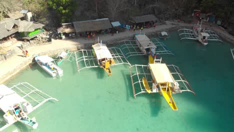 Aerial-rising-drone-shot-from-people-standing-at-a-Paraw-boat-harbor,-in-a-turquoise-lagoon,-between-limestone-cliffs,-on-a-sunny-day,-at-Coron-island,-Philippines,-Asia