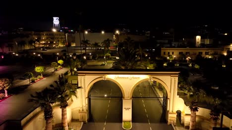Night-time-aerial-view-flying-over-illuminated-Paramount-pictures-Melrose-gate-movie-studio-lot,-Los-Angeles,-California