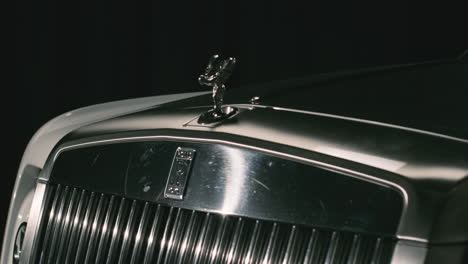 Front-bumper-with-large-shiny-grill-and-iconic-hood-ornament-of-Rolls-Royce-car,-indoor-studio