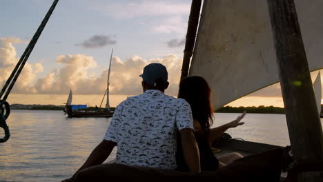 A-couple-watches-the-sunset-while-sailing-on-a-traditional-Swahili-dhow-boat-in-Lamu,-Kenya
