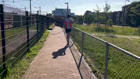 Running-male-trail-runner-followed-along-train-tracks-on-walk-path-over-a-viaduct