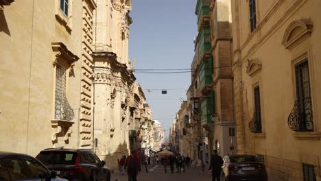 Narrow-street-in-the-capital-city-with-car-and-people-traffic,-Wide-shot