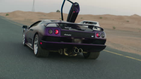Expensive-purple-vintage-Lamborghini-driving-on-road-surrounded-by-sandy-desert-in-Dubai