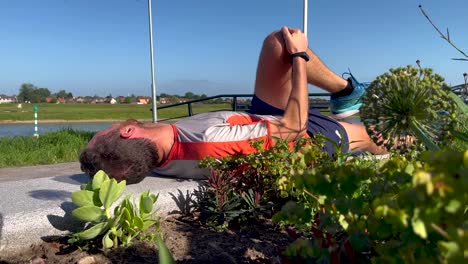 Cool-down-stretch-and-breathing-exercises-after-training-run-session-of-a-male-trail-runner-laying-on-public-bench-beside-vegetation