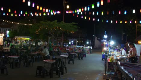 Shot-of-roadside-food-stalls-with-many-customers-enjoying-food-in-Nan-city,-Thailand-at-night-time