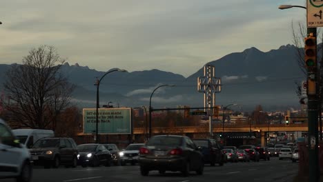 Cars-speed-down-a-busy-Vancouver-street-with-a-view-of-the-mountains-and-the-East-Van-sign