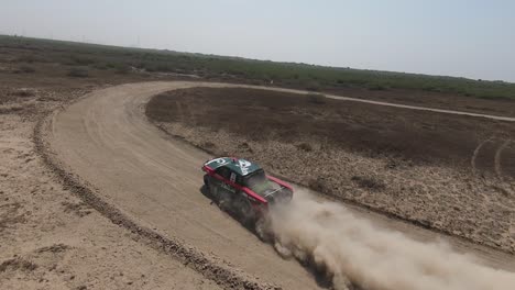 Aerial-Tracking-Shot-From-Behind-View-Of-Dust-Trails-From-Rally-Jeep-Car-Driving-Around-Curve-At-Hub-Rally-Cross-2023,-Slow-Motion