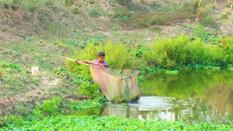 Zeitlupenaufnahme-Eines-Bengalischen-Jungen,-Der-Mit-Einem-Großen-Netz-Vegetation-Aus-Einem-Teich-Erntet-Und-Die-Pflanzen-Beobachtet