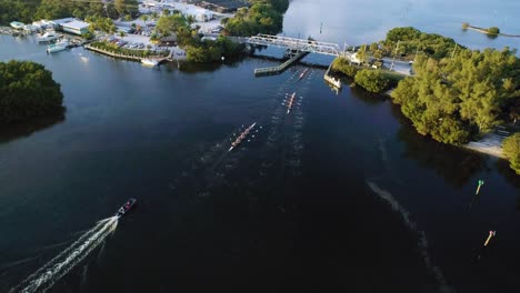 Aerial-Shot-of-Rowing-Crew-Approaching-a-Bridge-at-Sunset