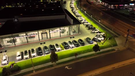 Illuminated-Mercedes-Benz-car-dealership,-Valencia,-California-night-time-aerial-view-rising-above-luxury-showroom