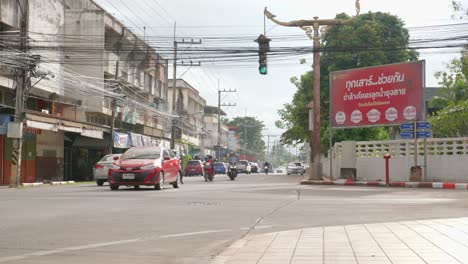Low-angle-shot-of-car-and-bike-movement-along-the-asphalt-road-in-Nan-city,-Thailand-on-a-sunny-day