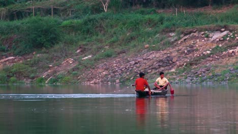 Two-fisherman-boy-dropping-fishing-net-in-river-from-canoe-boat-in-Bangladesh