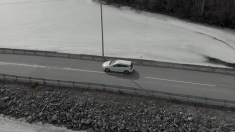 Drone-following-car-driving-on-road-across-water-in-winter-landscape