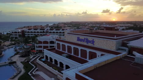 Hotel-De-Hard-Rock-En-Cancún,-México,-Mostrado-Desde-El-Punto-De-Vista-De-Un-Dron-Y-Una-Puesta-De-Sol-Al-Fondo