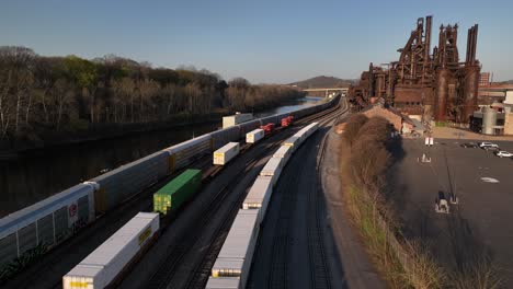 An-aerial-view-of-cargo-trains-in-Bethlehem,-Pennsylvania-on-a-sunny-day,-with-the-Bethlehem-Steel-plant-in-the-background