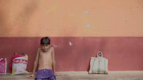 Young-Indian-boy-after-bath-sitting-near-a-wall-with-wet-pant-and-bare-chest,-slow-motion