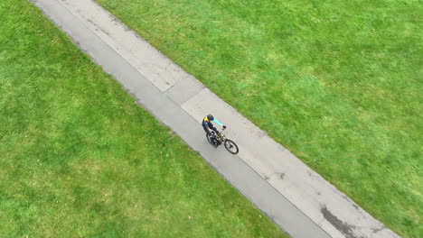 Radfahrer-Fährt-Fahrrad-Auf-Einem-Rad-Auf-Der-Strecke-Im-Grünen-Park-Und-Verfolgt-Drohnenaufnahme