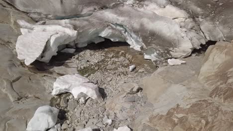 Aerial-shot-of-glacial-ice-cave-with-river-in-Swiss-Alps