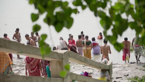 People-bathing-and-swimming-in-river-bank-of-Ganga,-Rani-Rashmoni-ghat,-shot-through-leaves-of-tree,-slow-motion