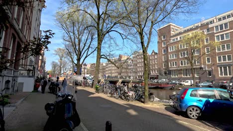 POV-Walking-Along-Amsterdam-Street-Beside-Canal-Past-Parked-Motorbikes-And-Vehicles