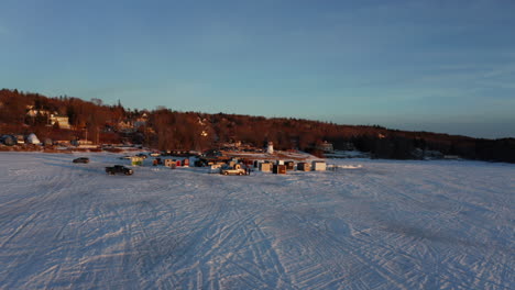 Scenic-aerial-view-of-an-ice-fishing-village-on-a-frozen-lake-at-sunset