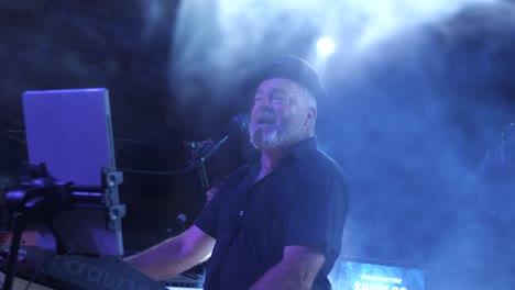 Energetic-singer-in-his-fifties-with-a-hat,-performing-on-stage-with-smoke-and-blue-lights