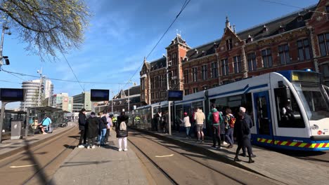 Tram-departs-outside-Amsterdam-Central-Station-in-sunlight,-static
