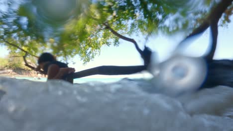 Daughters-on-tree-brunch-watching-the-waves-passing-underneath-them,-Mahe-Seychelles-slow-motion