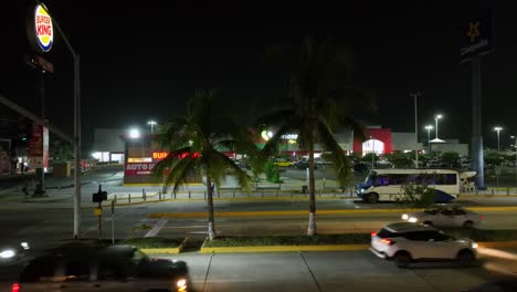 Tráfico-Que-Pasa-Por-La-Plaza-Salagua-Y-Restaurante-De-Comida-Rápida-Por-La-Noche-En-Manzanillo,-Colima,-México