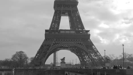 Monochrome-Shot-Of-Seine-River-Cruise-Sailing-Under-Crowded-Pont-de-Passy-With-Scenic-View-Of-Famous-Eiffel-Tower-In-Paris,-France