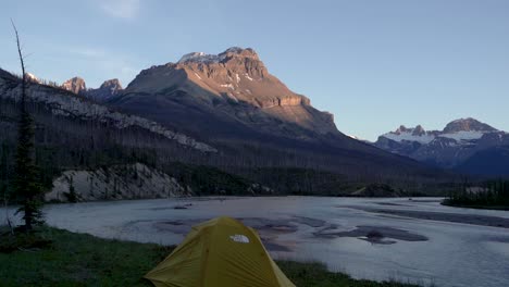 Tilt-down-reveal-shot-of-a-tent-in-front-of-the-Canadian-Rockies-during-the-sunset