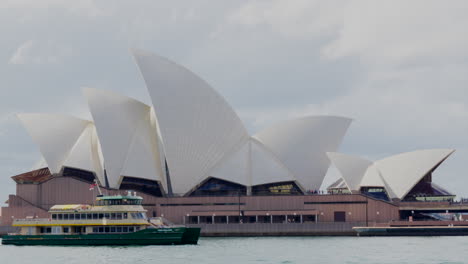 A-ferry-waving-the-indigenous-Aboriginal-flag-passes-by-the-opera-house-in-Sydney,-Australia