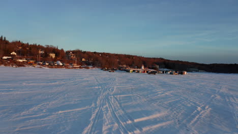 Luftaufnahme,-Die-Bei-Sonnenuntergang-Auf-Eisfischerhütten-Auf-Einem-Zugefrorenen-See-Zufliegt