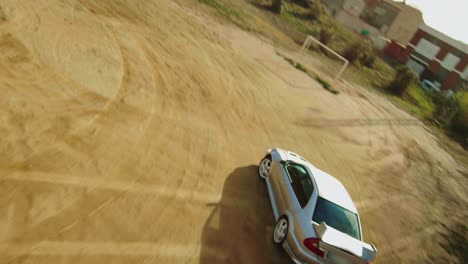 Intense-FPV-drone-chasing-a-stunt-car-driving-on-a-dirt-football-field