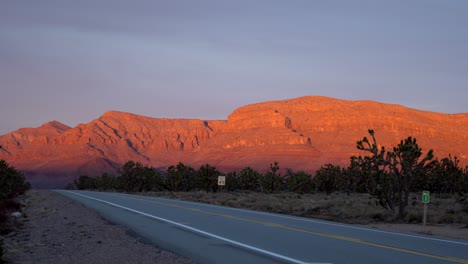 Car-driving-along-Joshua-trees-with-glowing-mountain-during-sunset
