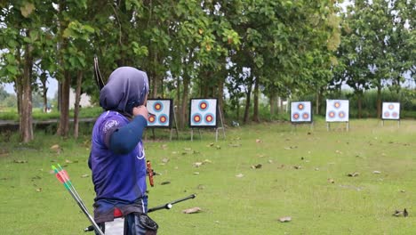 Indonesia---April,-2023-:-Asian-young-woman,-bow-or-arrows-aim-in-sports-field,-shooting-range,-hobby-or-performance-exercise,-weapon-in-target-training,-competition-or-practice
