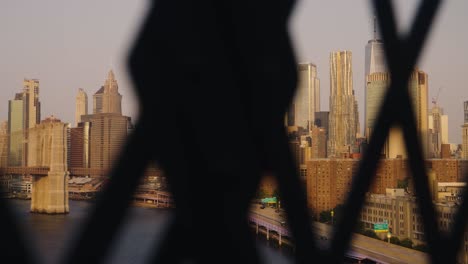 Panning-shot-showing-Skyline-of-New-York-an-River-behind-fence-holes-of-bridge-at-sunset