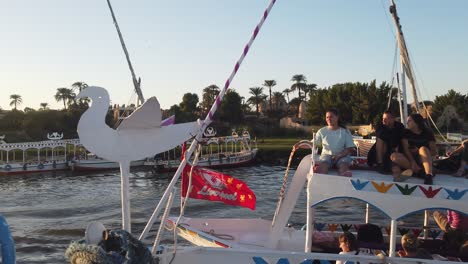 Slow-Motion-of-Tourists-sitting-on-Roof-of-egyption-Local-felucca-tour-boat-on-Nile-river-heading-to-Banana-Island-in-Luxor,-Egypt