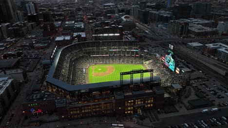 Coors-Field-in-Denver-lit-up-with-floodlights-at-night,-aerial-arc