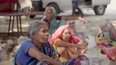 Poor-old-spiritual-Indian-women-sitting-on-ground-outside-a-temple,-rack-focus,-slow-motion
