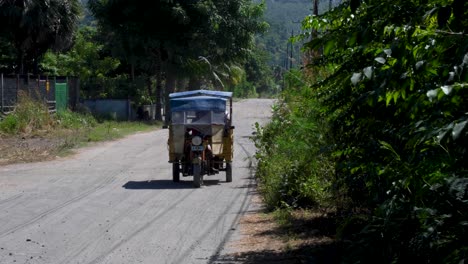 A-local-tuktuk-taxi-driving-along-a-bumpy,-dusty-gravel-road-on-the-remote-tropical-Atauro-Island-in-Timor-Leste,-Southeast-Asia