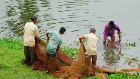 Fishermen-remove-tangled-weeds-from-their-fishing-nets-on-the-Surma-Riverbank,-Bangladesh