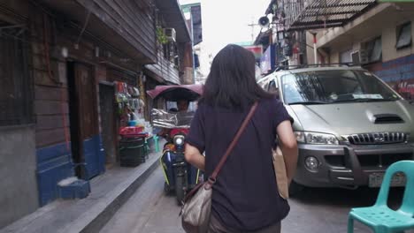 Tracking-follow-rear-view-of-woman-walking-through-busy-alley-carrying-package