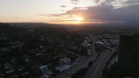 Aerial-view-passing-the-Comcast-NBC-Universal-city-plaza-tower,-toward-sunset-above-Studio-city-in-Los-Angeles,-USA